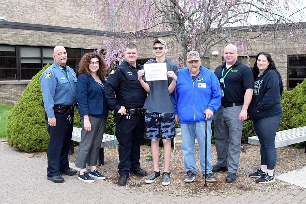 Timothy Kolka, his family and Brewster HS staff pose in front of BHS. Timothy holds his certificate of recognition
